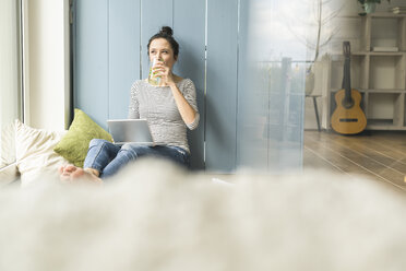 Woman sitting at the window at home working with laptop and drinking infused water - UUF17174