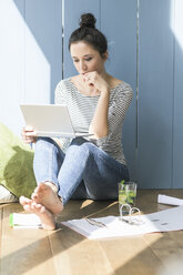 Woman sitting at the window at home working with laptop and file folder - UUF17176