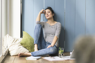 Relaxed woman sitting at the window at home having a break - UUF17178