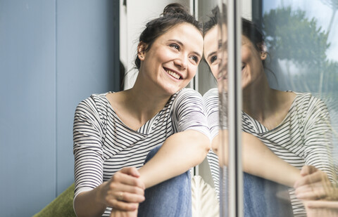 Lächelnde Frau schaut zu Hause aus dem Fenster, lizenzfreies Stockfoto