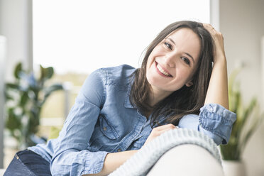 Portrait of happy woman sitting on the couch at home - UUF17223