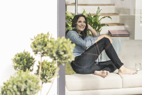 Happy woman sitting on couch behind windowpane at home stock photo