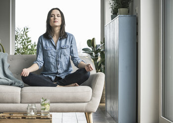Woman sitting on the couch at home in yoga pose - UUF17238