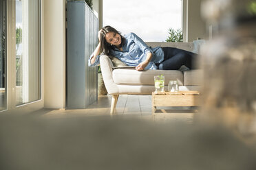 Happy woman lying on the couch at home using tablet - UUF17240