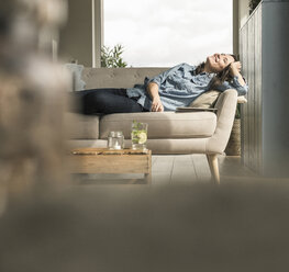 Happy woman lying on the couch at home - UUF17241