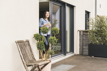 Smiling woman standing at terrace door at home with healthy drink - UUF17247