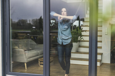 Serious woman standing behind terrace door at home - UUF17249