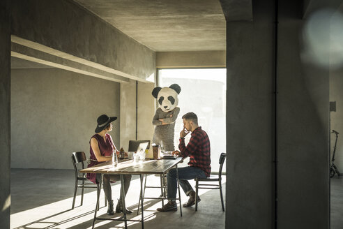 Woman with panda mask watching colleagues in office - MJRF00150