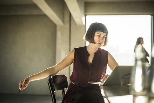 Pensive woman sitting in loft office, using laptop - MJRF00151