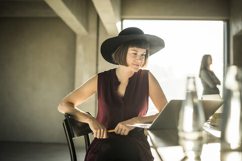 Woman with hat sitting in loft office, using laptop stock photo