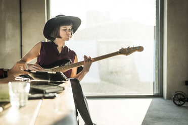 Frau mit Hut sitzt im Büro und spielt Gitarre - MJRF00155