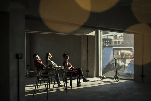 Eine Gruppe von Kreativen sitzt in ihrem Büro, schaut aus dem Fenster und genießt die Sonne - MJRF00164