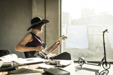 Frau mit Hut sitzt im Büro und spielt Gitarre - MJRF00166