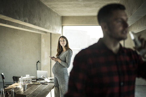 Smiling woman with smartphone watching colleague in office - MJRF00171