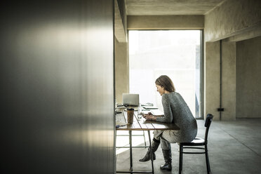 Frau sitzt im Büro und benutzt ein Smartphone - MJRF00174