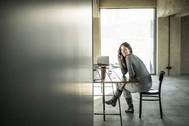 Woman sitting in office, using smartphone - MJRF00176