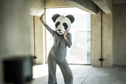 Frau mit Pandamaske steht im Büro und macht ein Selfie, lizenzfreies Stockfoto