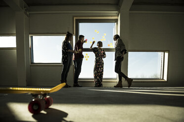 Creative professinal standing in office, brainstorming, putting sticky notes on a window - MJRF00189