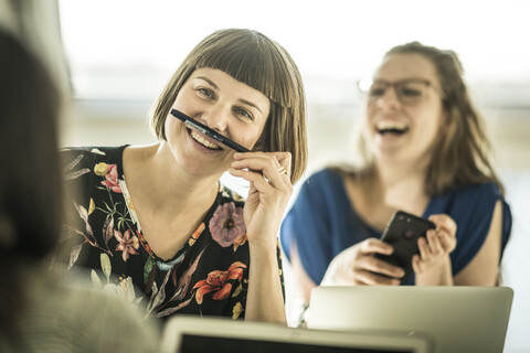 Kollegen, die sich im Büro mit einem Bleistiftschnurrbart amüsieren, lizenzfreies Stockfoto