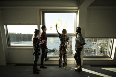 Kreativer Professor, der im Büro steht und ein Brainstorming durchführt, indem er Klebezettel an ein Fenster klebt - MJRF00203