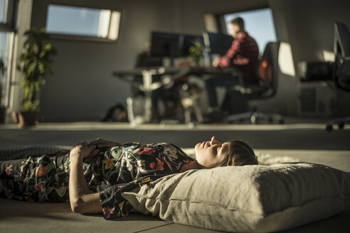 Frau, die ein Nickerchen macht, auf einem Kissen auf dem Büroboden liegend - MJRF00210