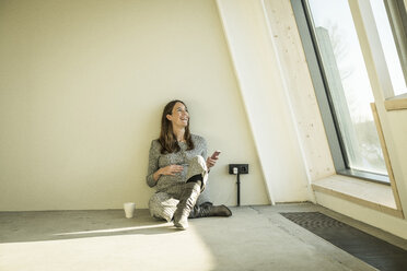 Pregnant woman drinking tea, sitting on floor of her new home - MJRF00212