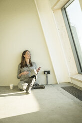 Pregnant woman drinking tea, sitting on floor of her new home - MJRF00213