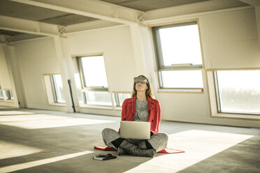 Pregnant busnesswoman sitting on floor of new office rooms, using VR goggles and laptop - MJRF00219