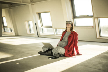 Pregnant busnesswoman sitting on floor of new office rooms, using VR goggles and laptop - MJRF00220