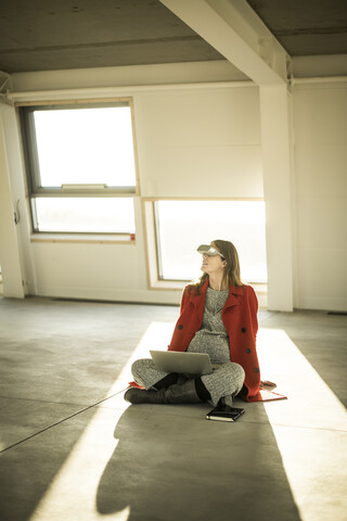 Schwangere Geschäftsfrau auf dem Boden neuer Büroräume sitzend, mit VR-Brille und Laptop, lizenzfreies Stockfoto