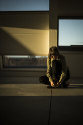 Businesswoman sitting on office floor at sunset, using smartphone - MJRF00227