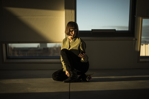 Geschäftsfrau sitzt bei Sonnenuntergang im Büro und benutzt ihr Smartphone, lizenzfreies Stockfoto