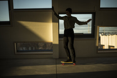 Geschäftsfrau, die bei Sonnenuntergang im Büro Skateboard fährt - MJRF00229