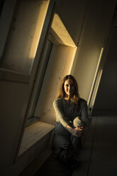 Frau am Bürofenster sitzend bei Sonnenuntergang, Porträt - MJRF00235
