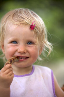 Portrait of blond little girl with bib and pink haipin eating sausage - GAF00139
