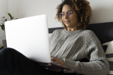 Frau sitzt auf dem Bett, benutzt einen Laptop und surft im Internet - FMOF00546