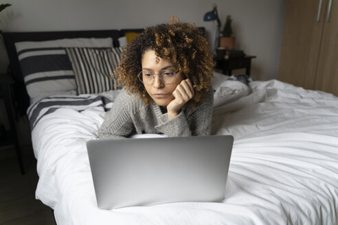 Frau liegt auf dem Bett, benutzt einen Laptop und surft im Internet - FMOF00547
