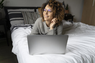 Woman lying on bed, using laptop, surfing the net - FMOF00548