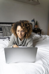 Frau liegt auf dem Bett, benutzt einen Laptop und surft im Internet - FMOF00549