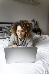 Woman lying on bed, using laptop, surfing the net - FMOF00549