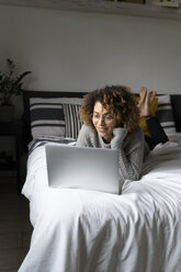 Frau liegt auf dem Bett, benutzt einen Laptop und surft im Internet - FMOF00550