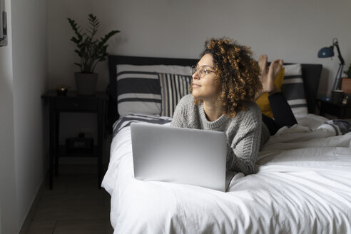 Frau liegt auf dem Bett, benutzt einen Laptop und surft im Internet - FMOF00551