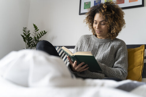 Frau sitzt auf dem Bett und liest ein Buch - FMOF00553