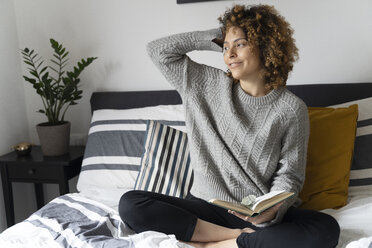 Frau sitzt auf dem Bett und liest ein Buch - FMOF00555