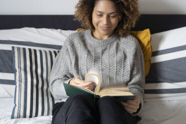 Woman sitting on bed, reading book - FMOF00556