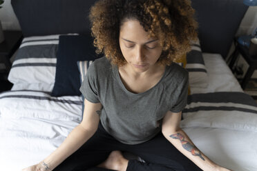 Woman practicing yoga, sitting on bed, meditating - FMOF00560