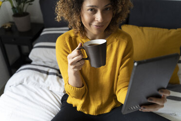Frau auf dem Bett sitzend, eine Pause machend, Kaffee trinkend, auf ein digitales Tablet tretend - FMOF00571
