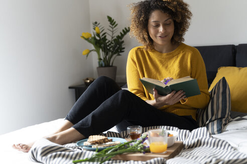 Frau sitzt auf dem Bett, frühstückt gesund und liest ein Buch - FMOF00579