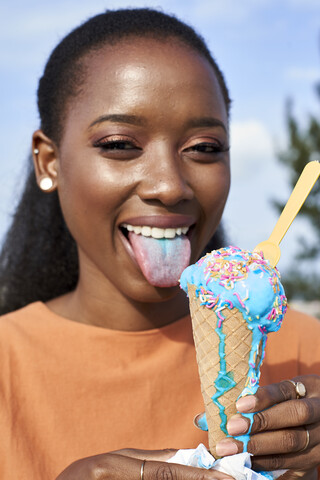 Porträt einer jungen Frau mit hellblauem Eis, die ihre Zunge herausstreckt, lizenzfreies Stockfoto