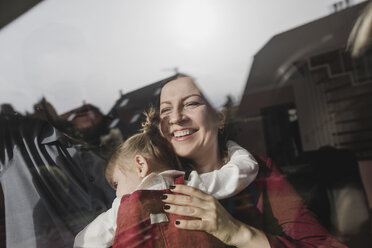 Glückliche Mutter, die ihre Tochter hinter einer Fensterscheibe umarmt - KMKF00824